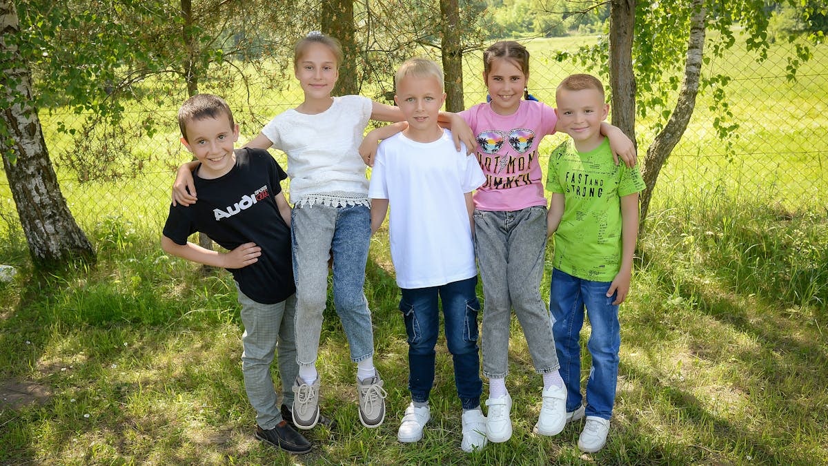 Five cheerful kids posing together in a sunny outdoor setting, embodying friendship and joy.